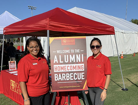 Greeters stand near the Alumni Homecoming Barbecue sign
