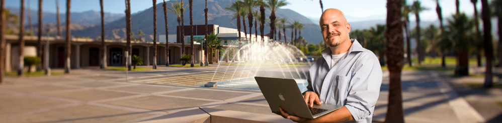 Male student using a laptop near the fountain